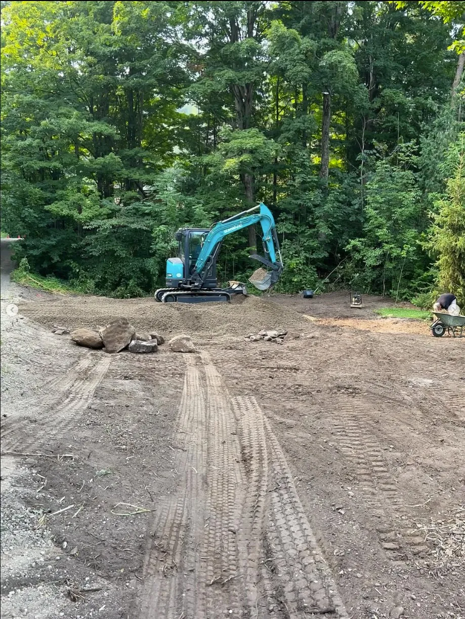 A mini excavator grading a gravel turnaround edged with fieldstone