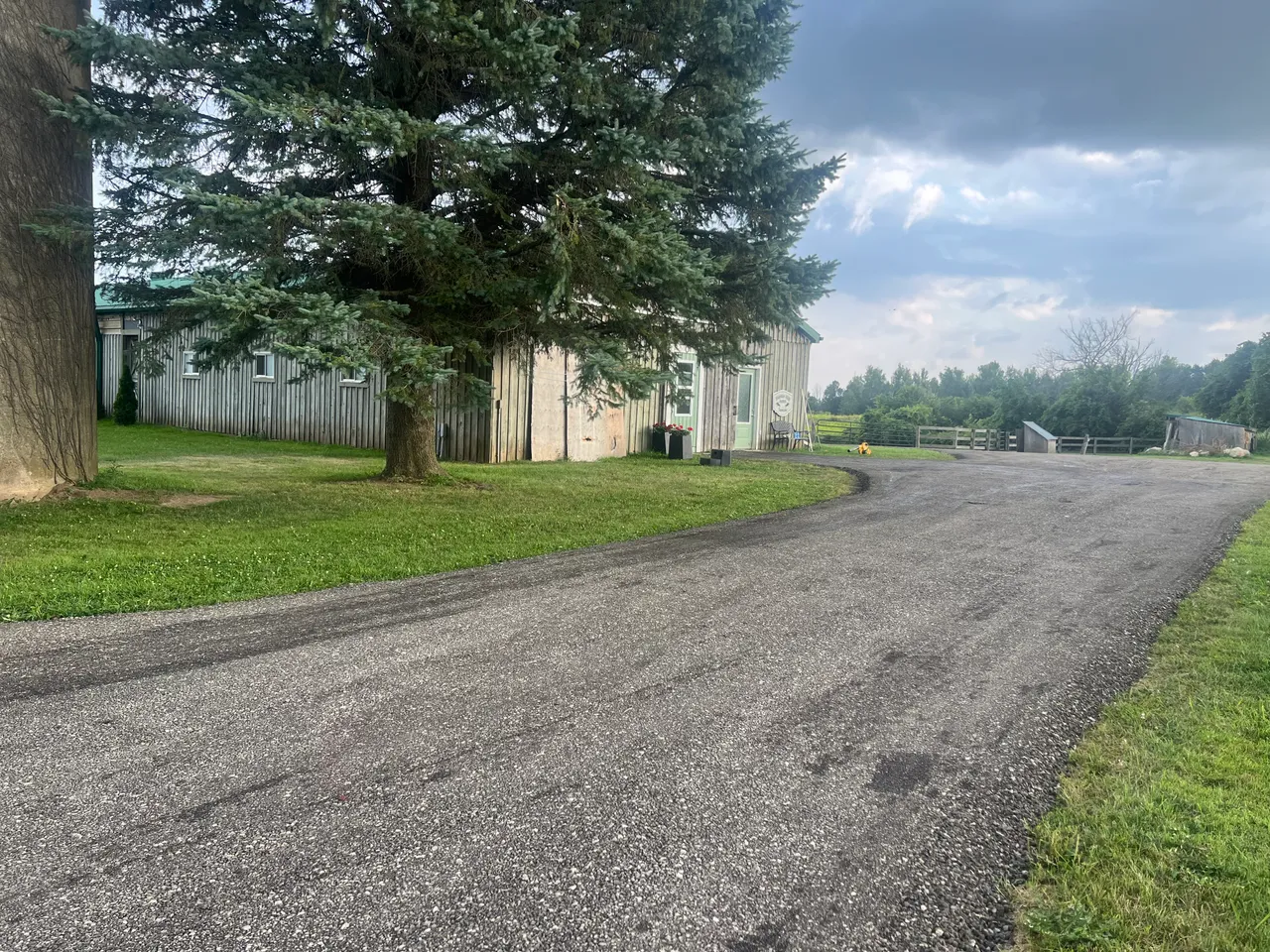 A finished laneway curving past a barn and evergreens