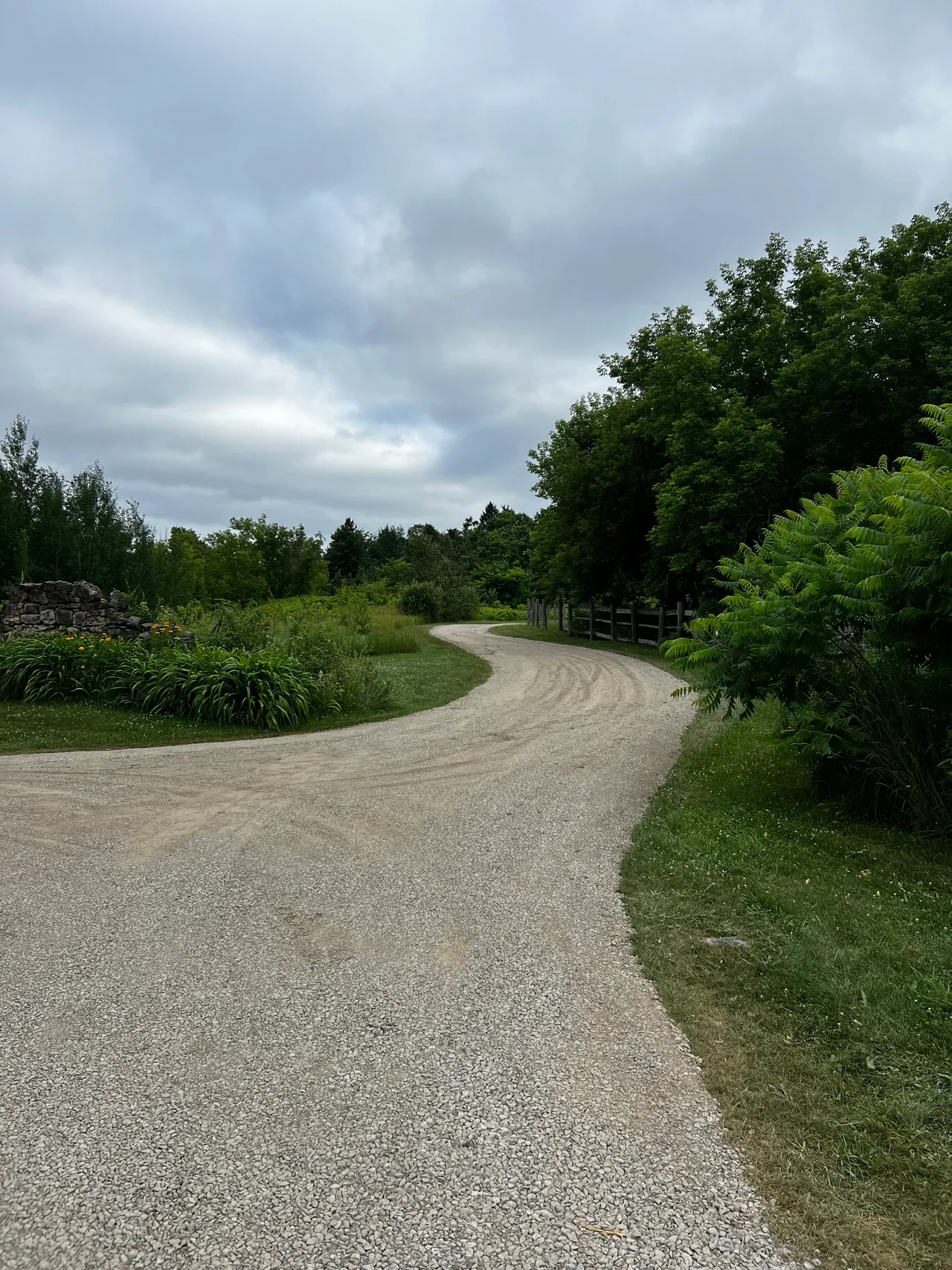 A finished gravel laneway curving past a fieldstone wall and fence