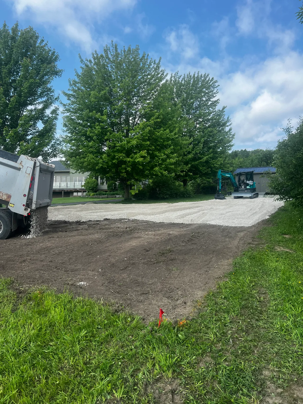 A dump truck spreading gravel to build a parking pad with an excavator alongside