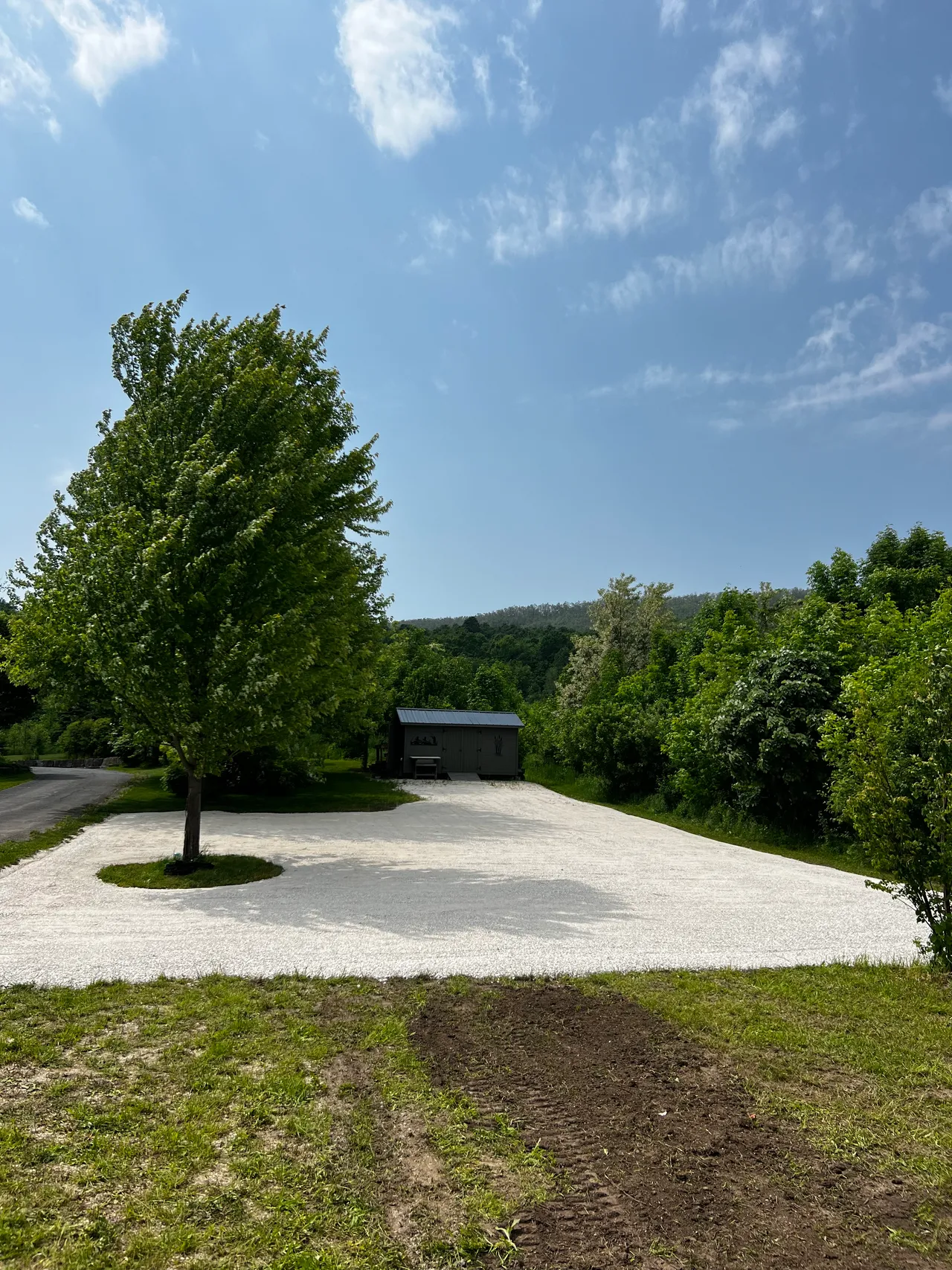 A freshly built white-gravel parking pad beside a small structure with hills behind